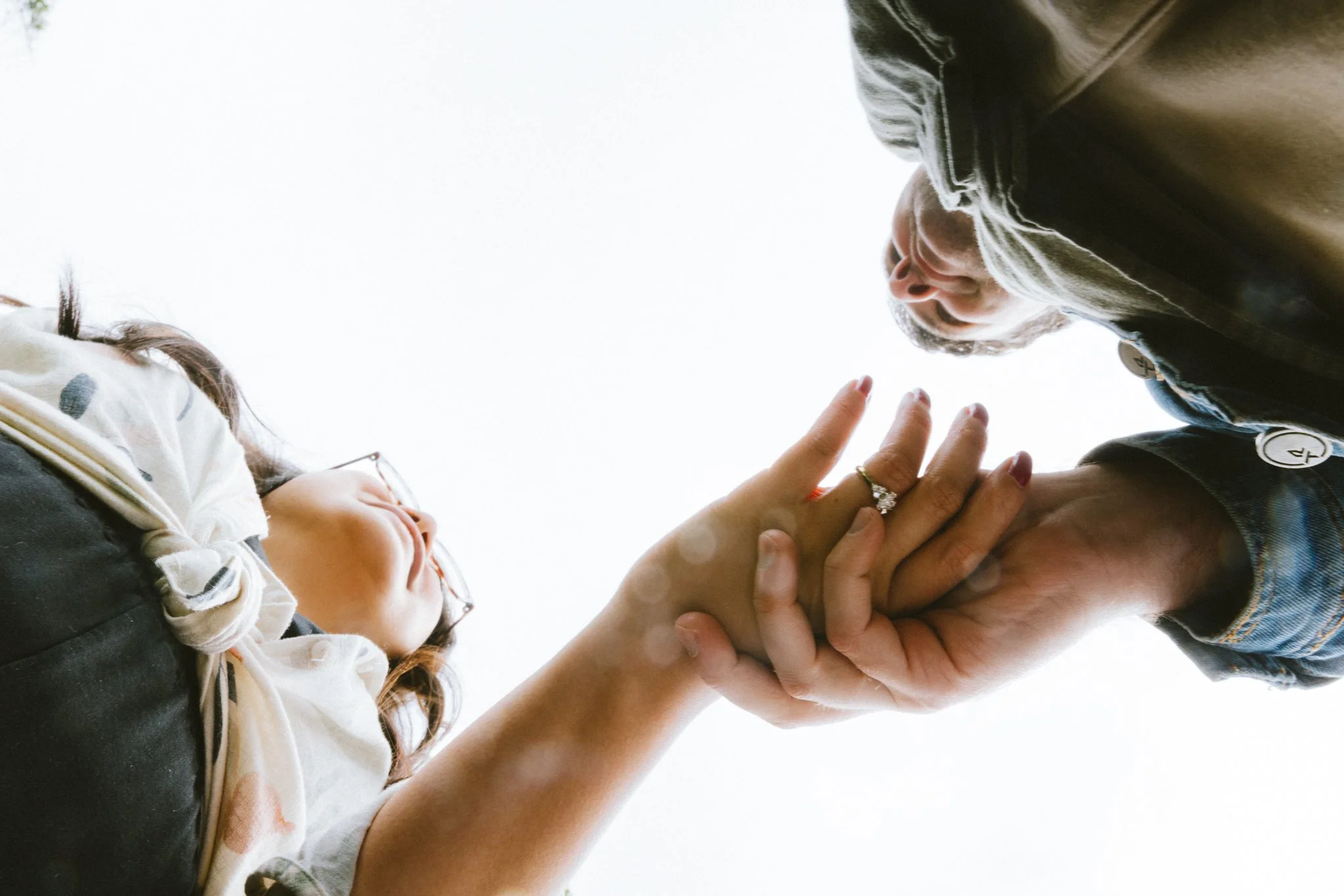 Ryan holding Mariel's hand up, engagement ring visible, both looking at each other from above in a low-angle frame