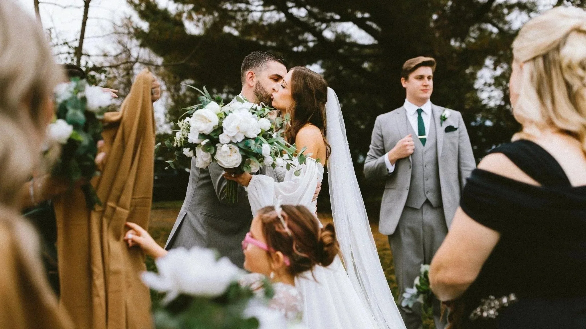 Bride and groom sharing their first kiss during an outdoor wedding ceremony surrounded by family and friends, documentary wedding photography by Love Story By Aira Maryland