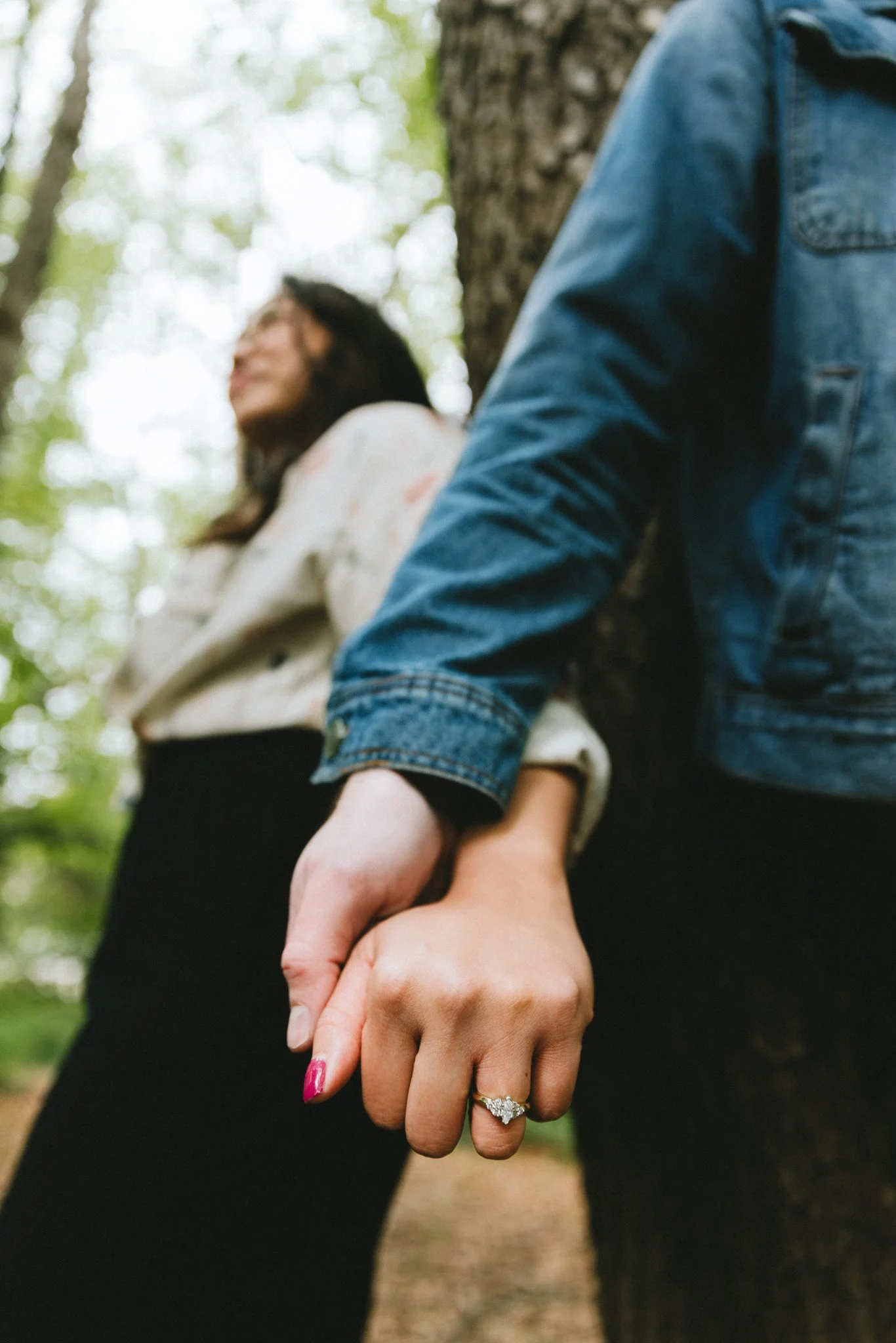  They standing back to back against a large tree trunk, holding hands, both looking away quietly 
