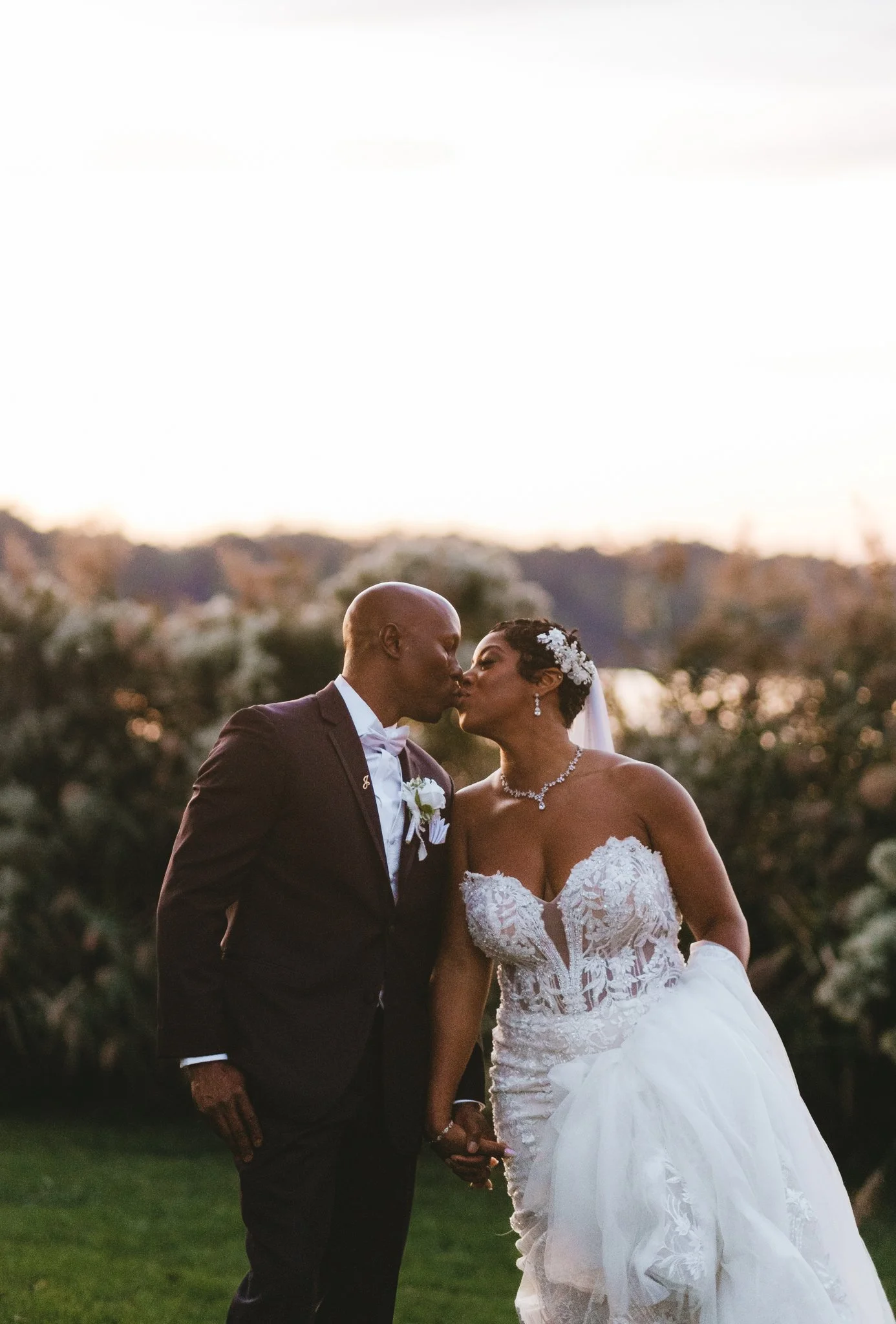 Bride and groom sharing a kiss, sky already shifting to deep gold and cool tones as the last light fades behind the trees
