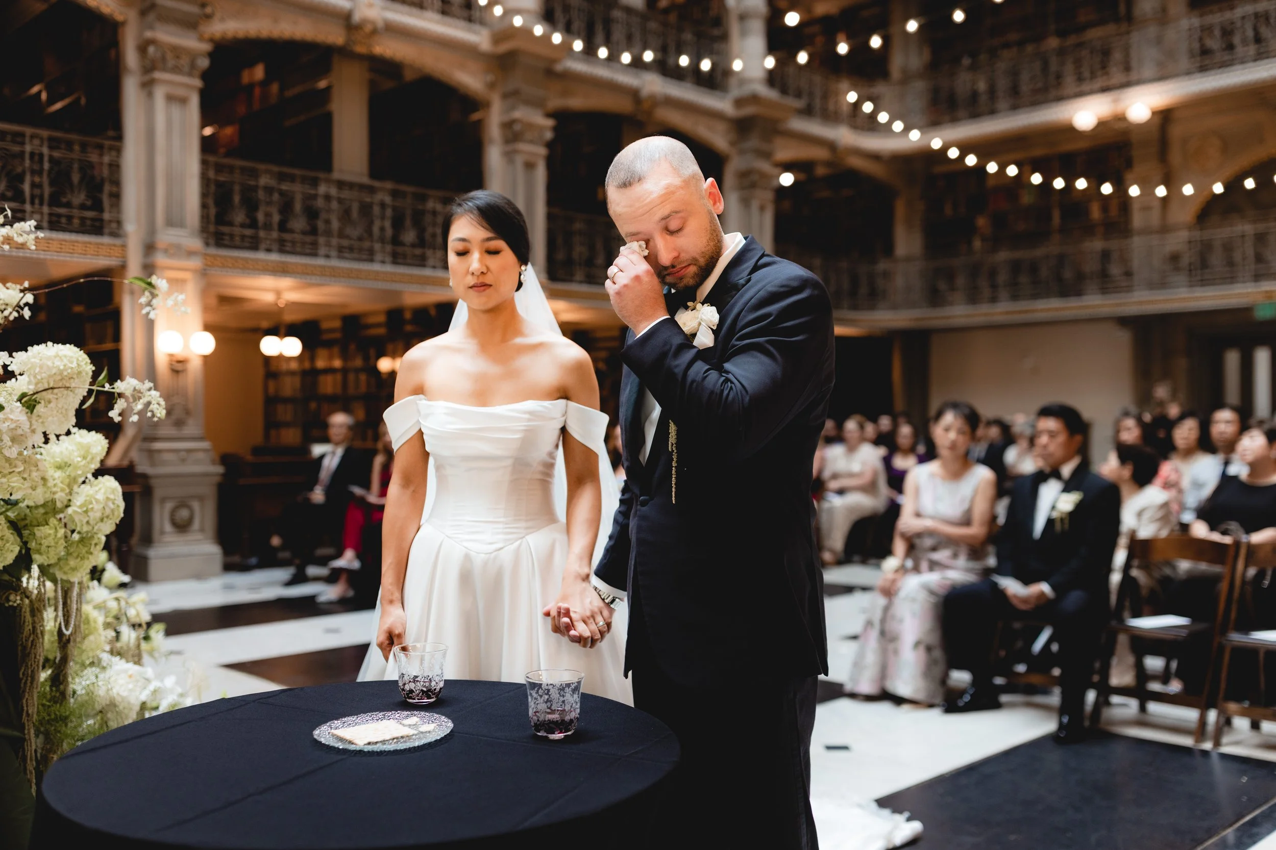 Emotional groom wiping tears during wedding ceremony at Peabody Library Baltimore, candid Maryland documentary wedding photography