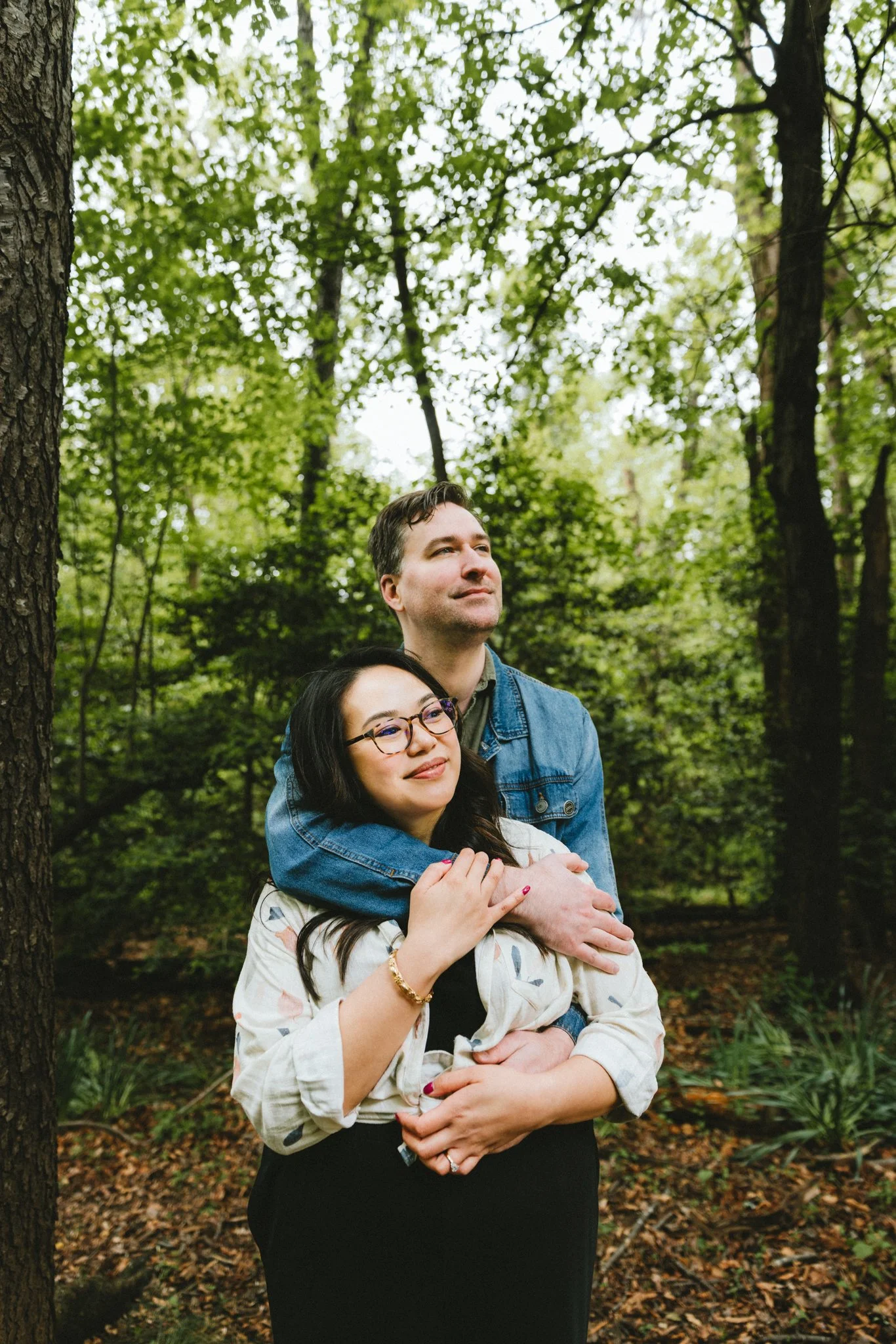  They embracing among the trees, Ryan holding her from behind as she looks up at the canopy 