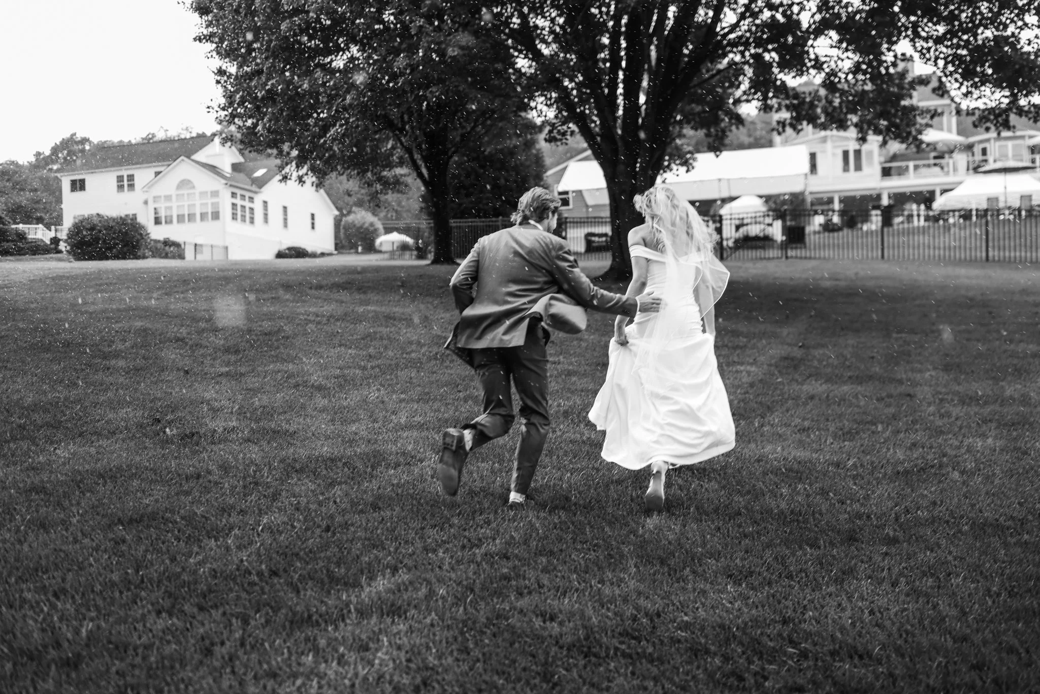 Bride and groom running through the rain laughing, black and white documentary wedding photography in Maryland