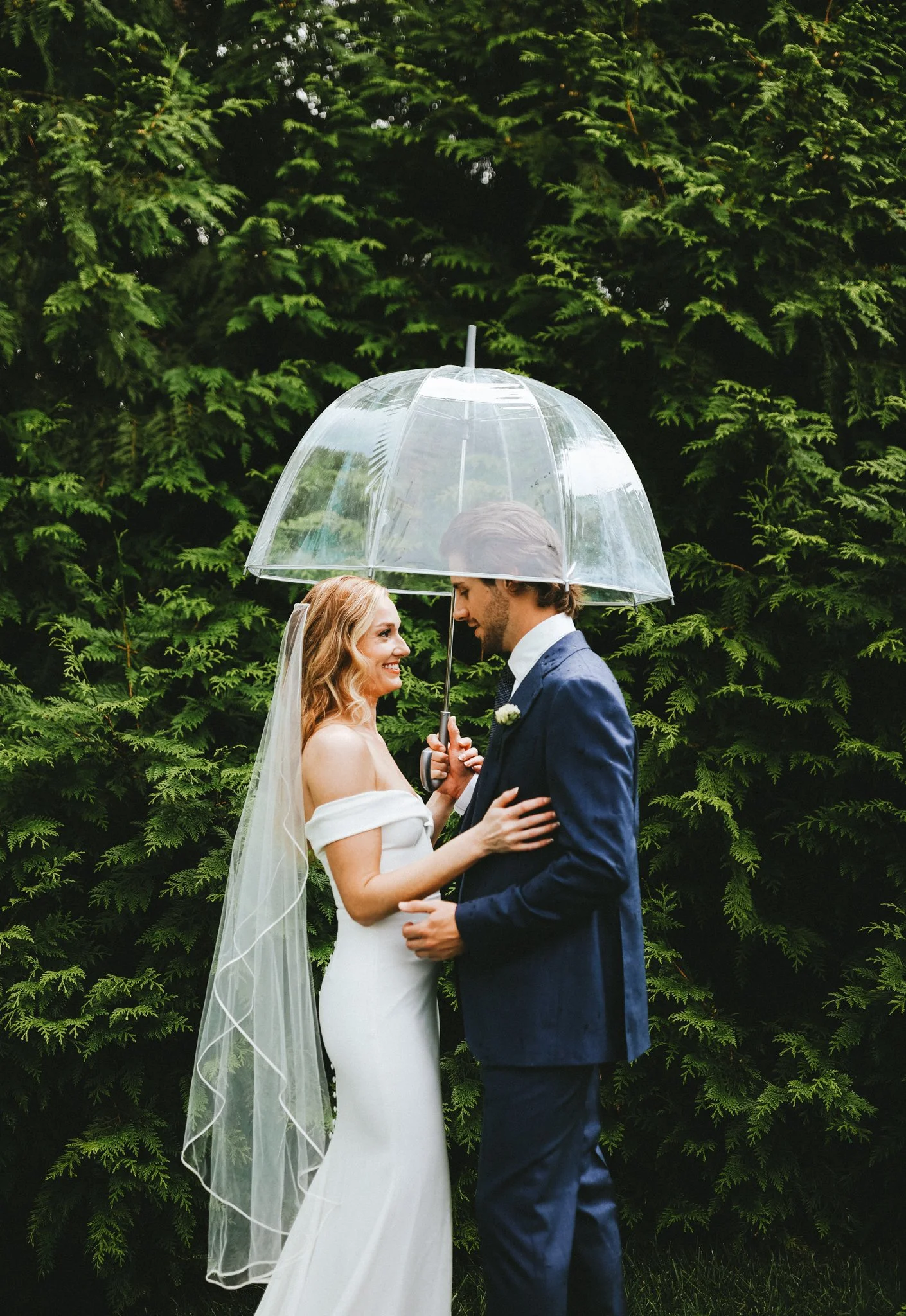 Bride and groom sharing a romantic moment under a clear umbrella in the rain