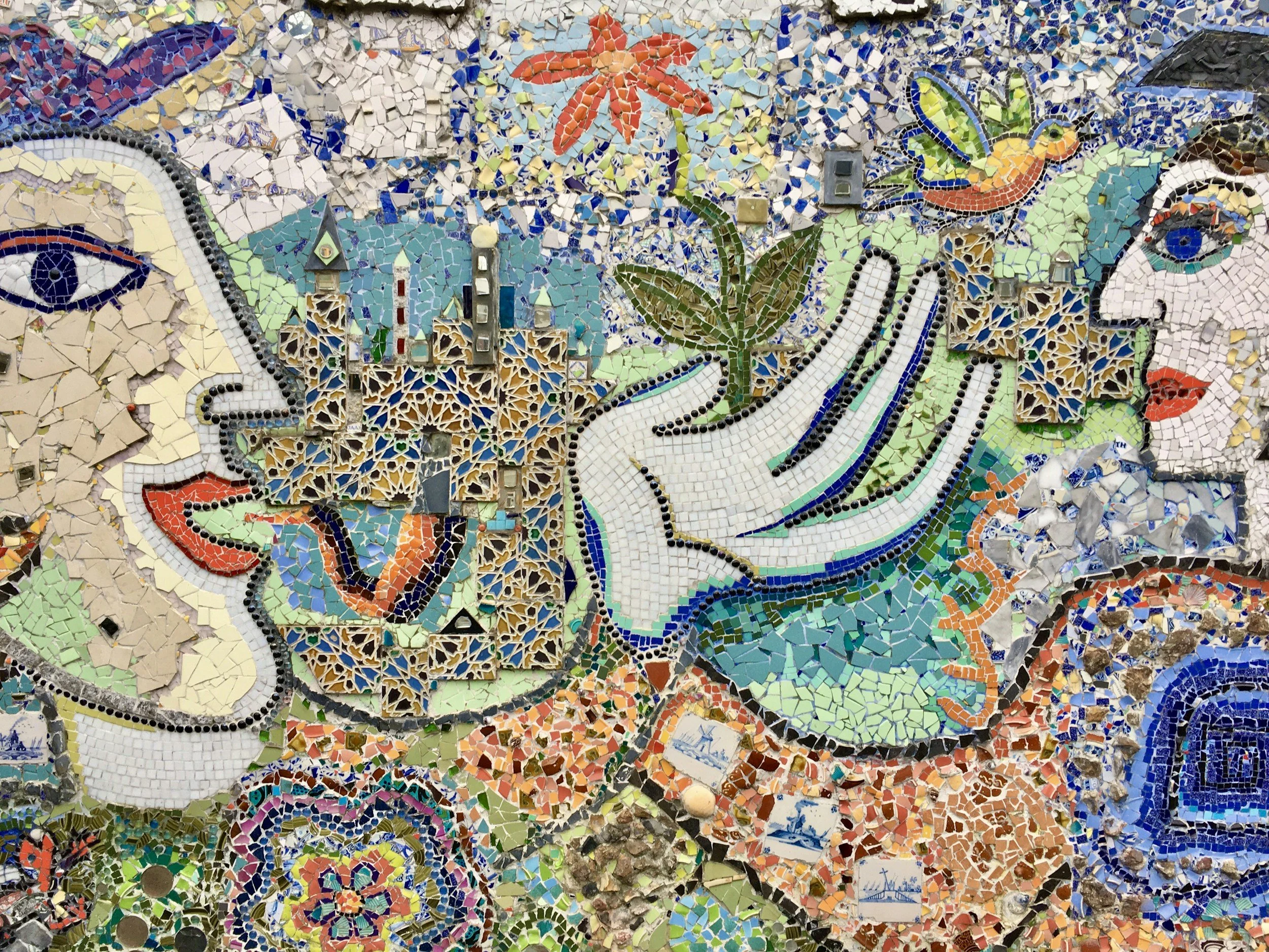 Close-up of a colorful mosaic mural depicting eyes, a flower in orange hues, and various geometric and organic shapes.