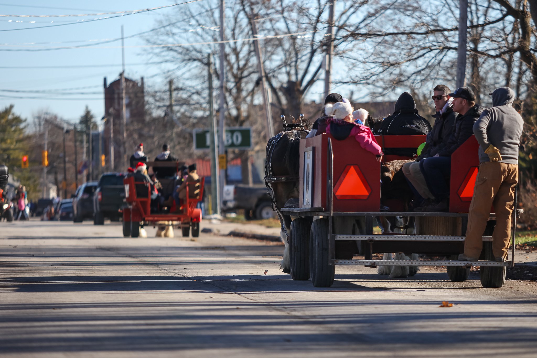 Horse-drawn carriages with passengers riding through a small town street decorated for Christmas