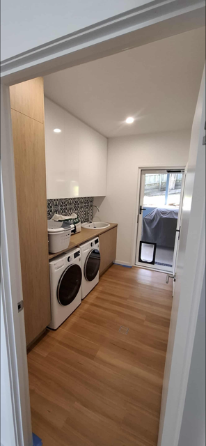 Laundry room with washer and dryer, white cabinets, wooden countertop, and door leading outside to a small porch.