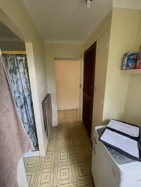 Laundry area with a top-loading washing machine, open lid, and papers on top, yellow walls, patterned vinyl flooring, a towel hanging on a wall, and a shower curtain visible on the left.