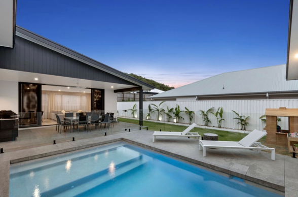 Backyard with a swimming pool, lounge chairs, patio area, and a house with large windows and sliding doors