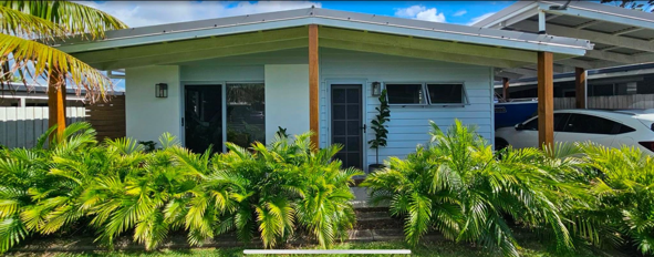 Front yard of a house with lush green bushes and a covered driveway, parked cars visible.