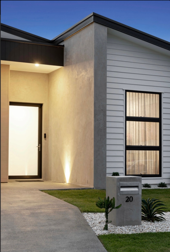 Modern house exterior with a concrete mailbox displaying the number 20, small desert plants, and a well-lit entrance during twilight.