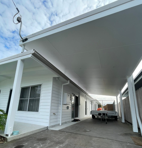 Back porch of a white house with a car parked underneath a large covered patio