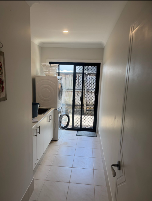 Laundry room with washing machine on top of a matching dryer, a countertop with a container, a basket on top of the washer, and a black door leading outside.