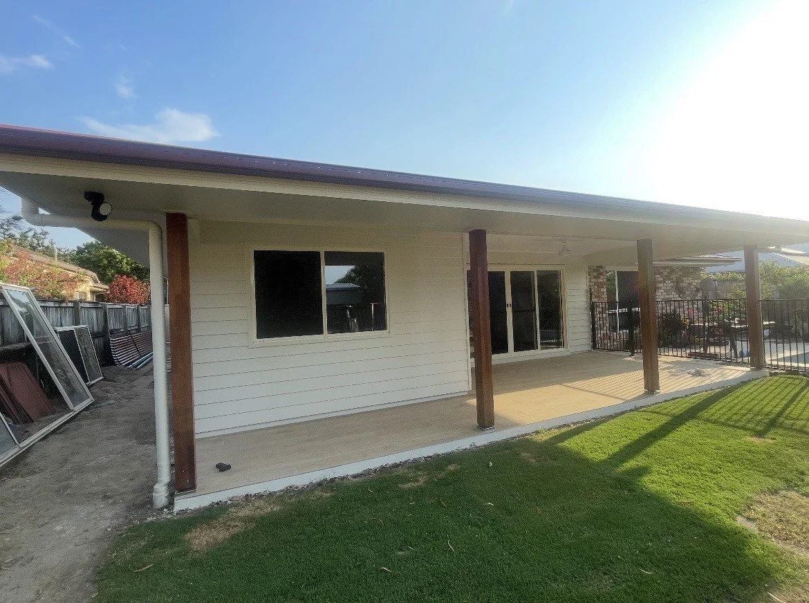 Back patio of a house with a covered porch, sliding glass doors, a window, and a grassy yard.