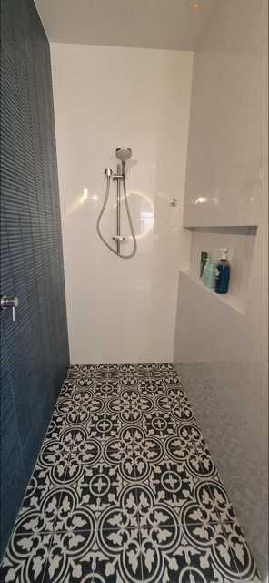 Empty shower with patterned tile floor, built-in shelf with soap bottles, and a showerhead on the wall.
