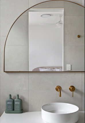 Bathroom with a large arched mirror, white sink, and two green soap dispensers.