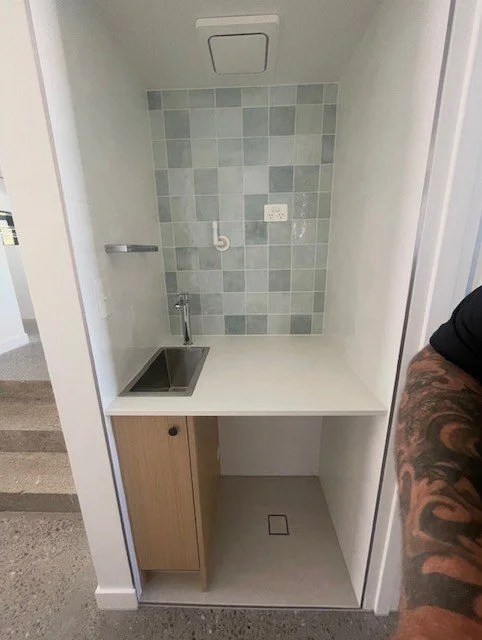 Small kitchenette with a stainless steel sink, a cabinet, tiled backsplash, and a faucet. A towel rack and electrical outlet are also visible.
