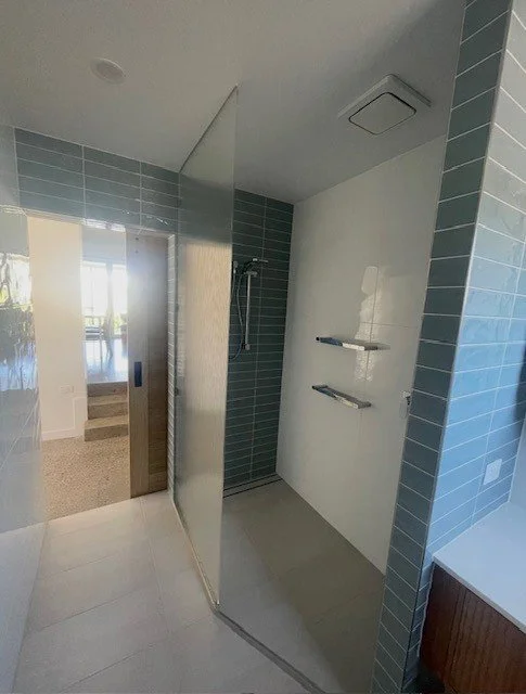 Empty walk-in shower with a showerhead and two floating shelves, surrounded by light blue tile walls and a partial mirror on the side.
