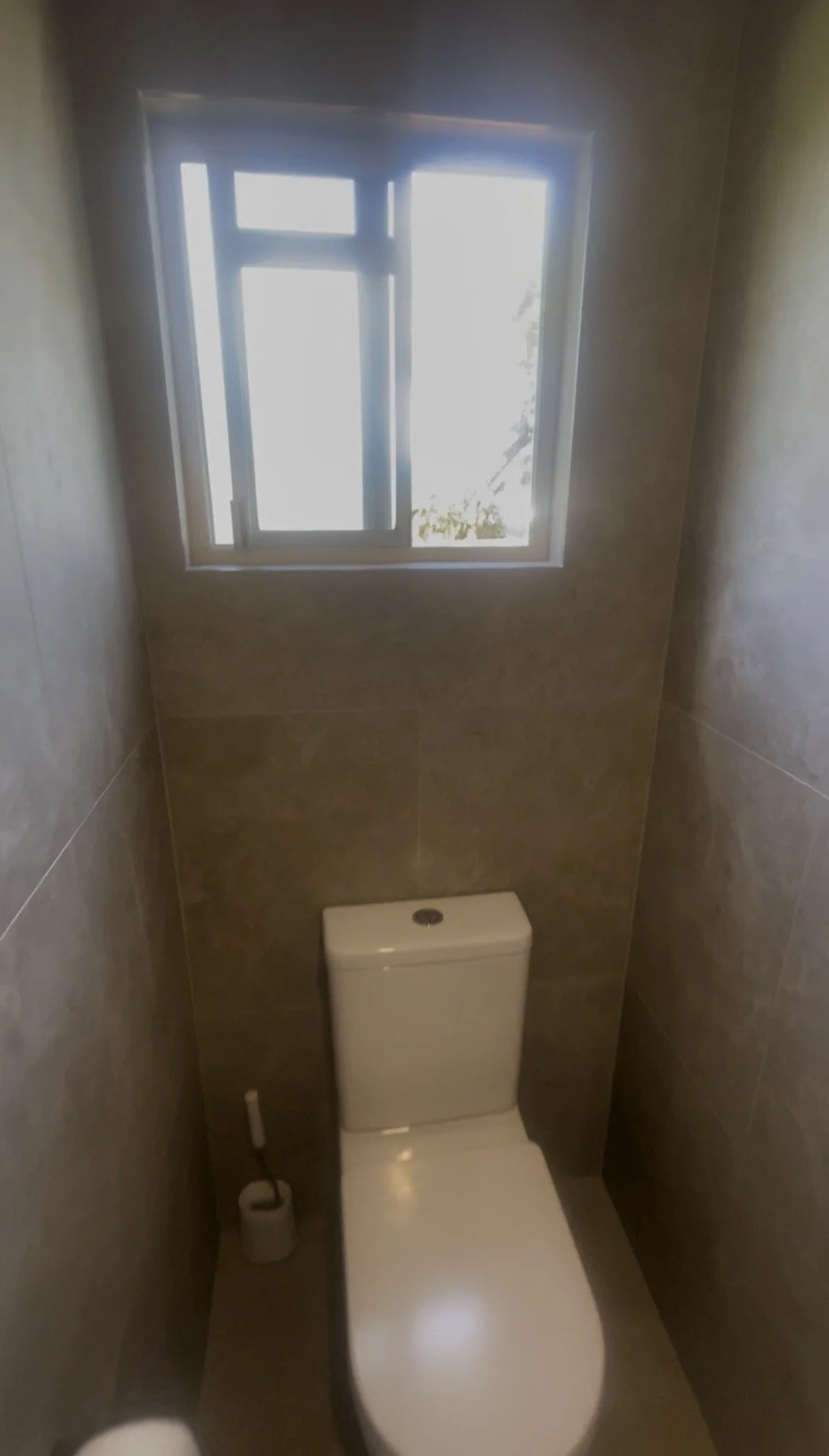 Small bathroom with a toilet placed against the back wall and a window above it allowing natural light in.