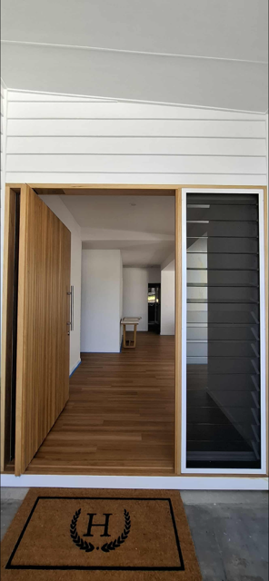 View through an open doorway showing a wooden floor, white walls, a small wooden table, and a hallway leading further inside a modern house.