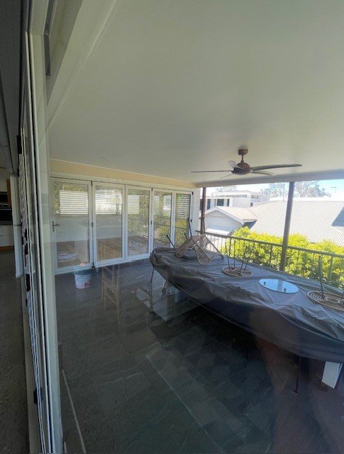 Enclosed balcony with a ceiling fan, sliding glass doors, a covered kayak, and a living space with a view of neighboring houses and trees.