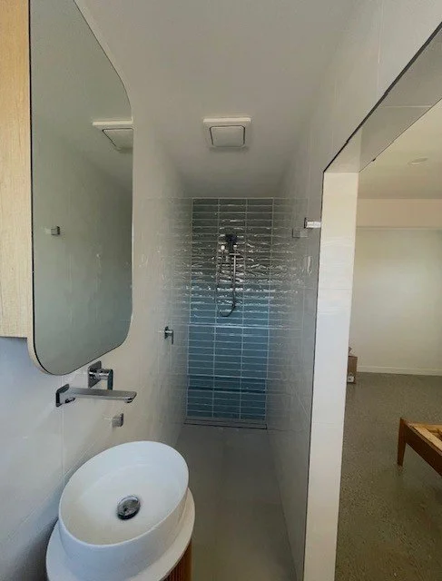 Minimalist bathroom with a round vessel sink, a large mirror, and a walk-in shower with blue tiles and a chrome showerhead