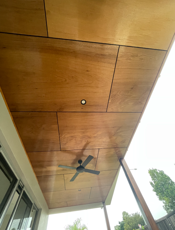 Image of a wooden ceiling with recessed lights and ceiling fan, outdoor view with trees, and part of a sliding glass door.