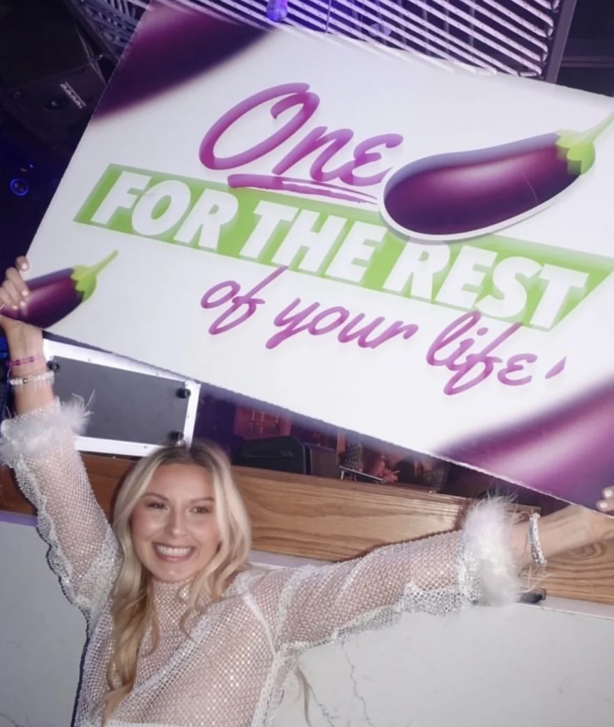 Woman smiling and holding a large sign that reads 'One for the rest of your life' with images of eggplants.