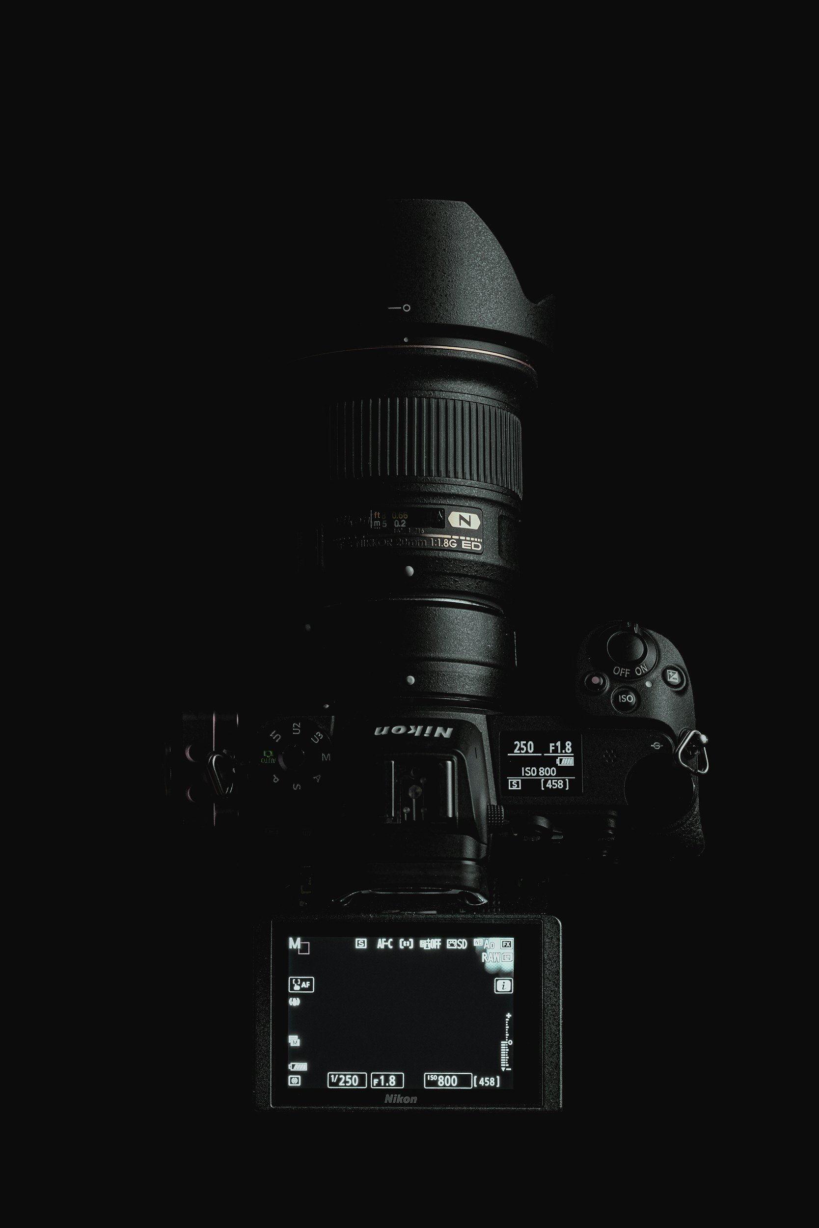 A Nikon camera with a large lens and a screen displaying camera settings in a dark environment.