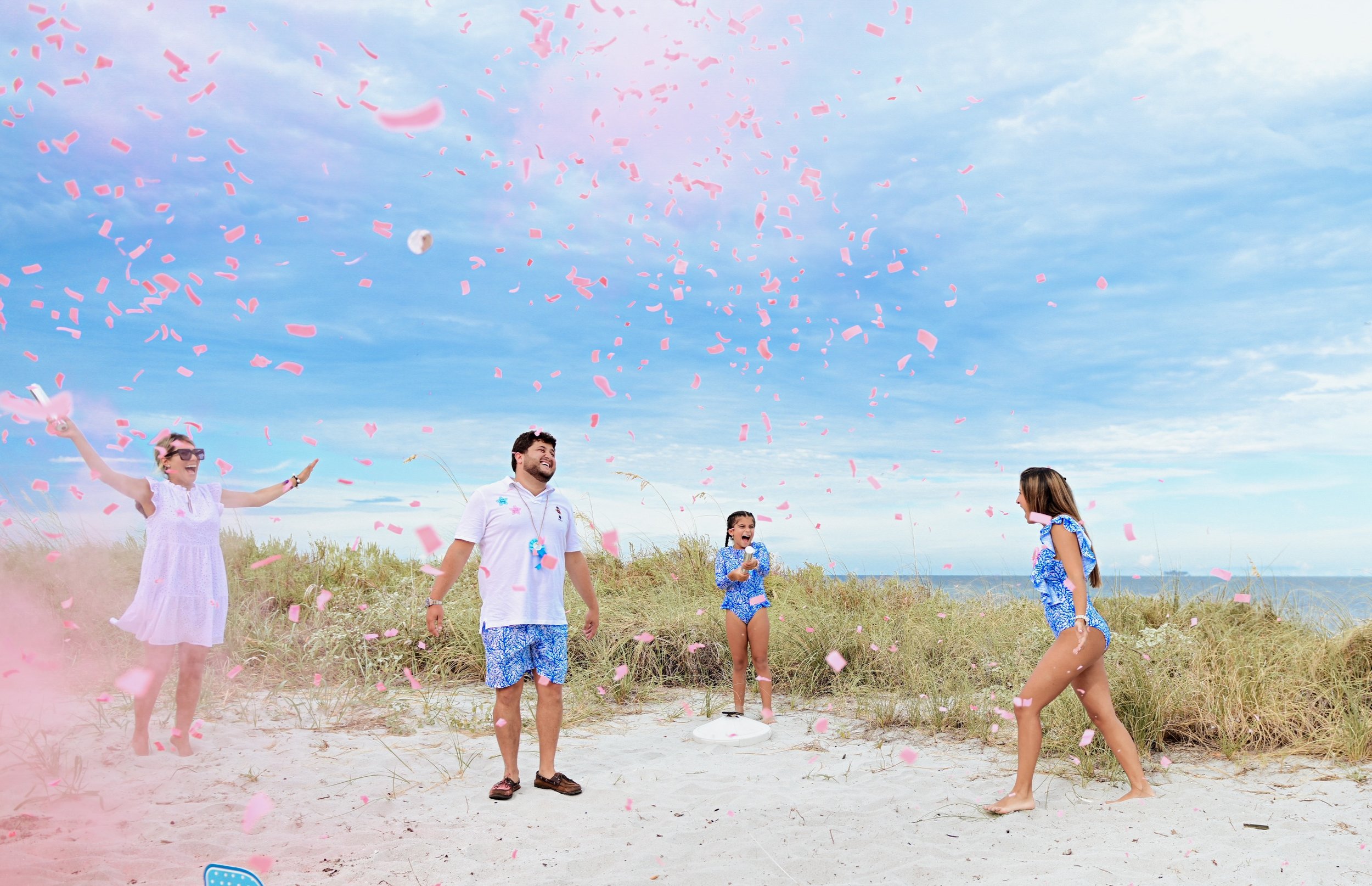 People celebrating on a beach with pink confetti and balloons, smiling and enjoying the outdoors.
