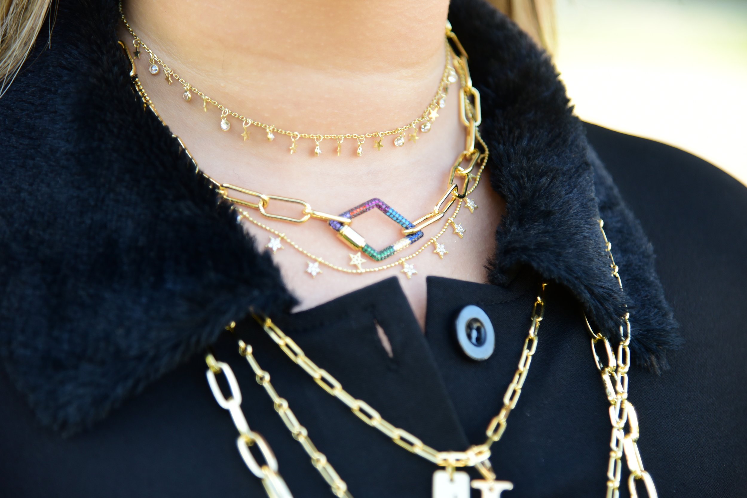 Close-up of a woman wearing layered gold necklaces with charms and a black fur coat.