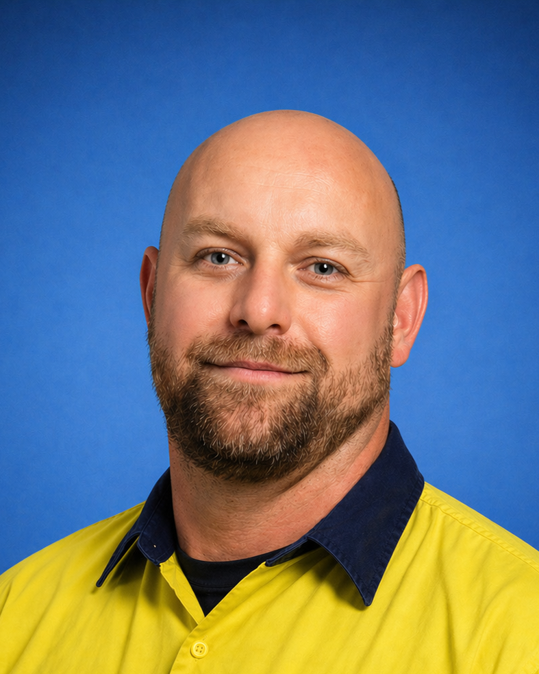 Portrait of a smiling bald man with a beard, wearing a blue collared shirt against a plain blue background.