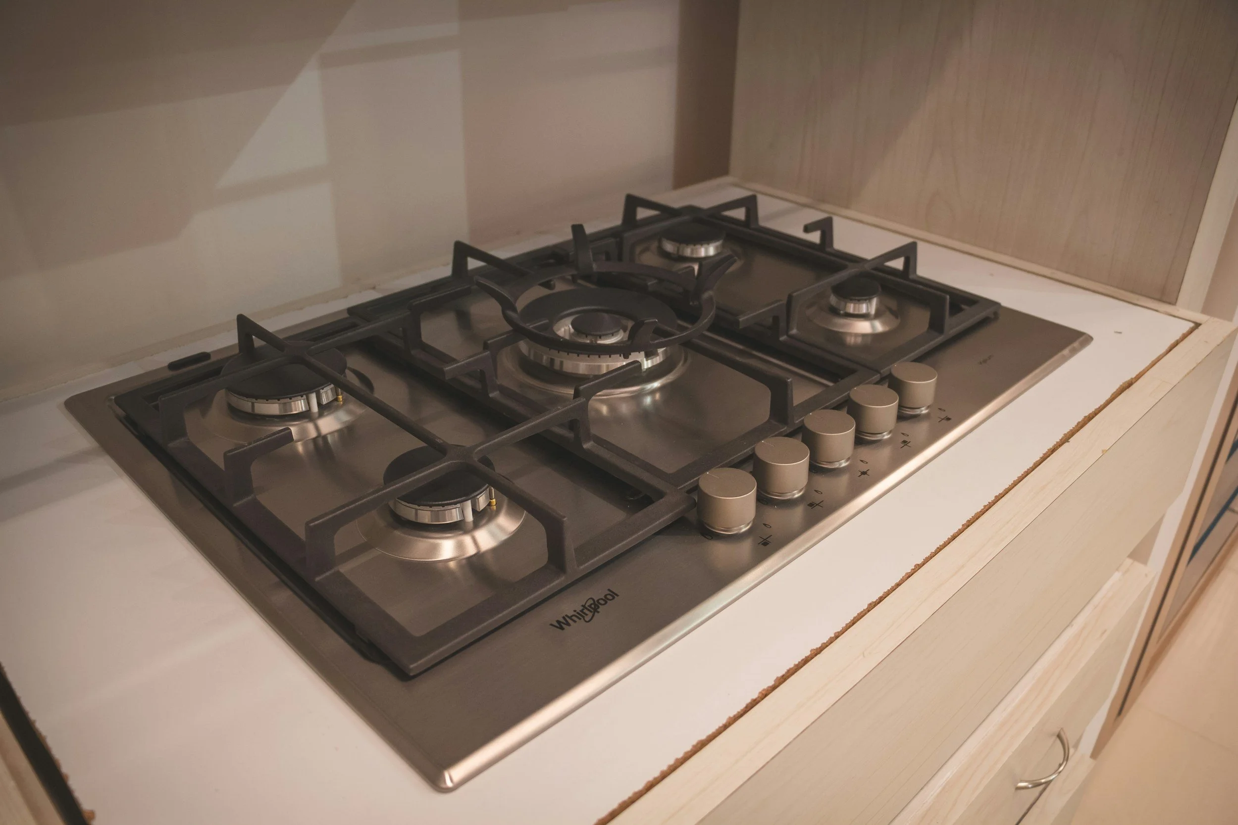 A stainless steel gas stove with four burners and control knobs on a white countertop with wooden cabinetry.