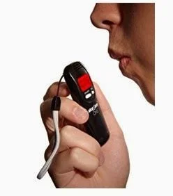 Person holding a breathalyzer device close to mouth for testing alcohol levels.