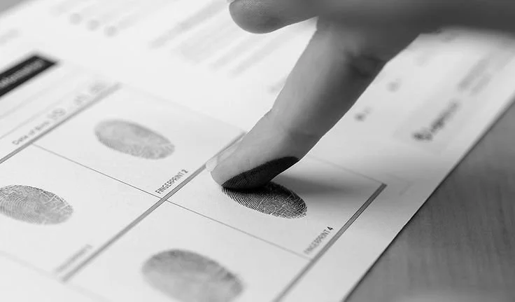 Close-up of a finger pressing a fingerprint on a document, with other fingerprint sections visible.
