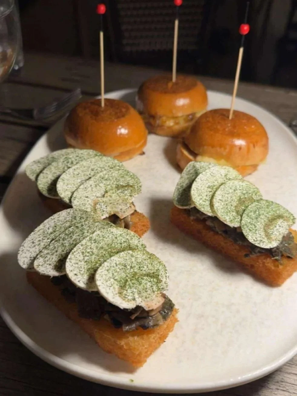Appetizers with sliders topped with potato chips and chopped garlic, served on a white plate.