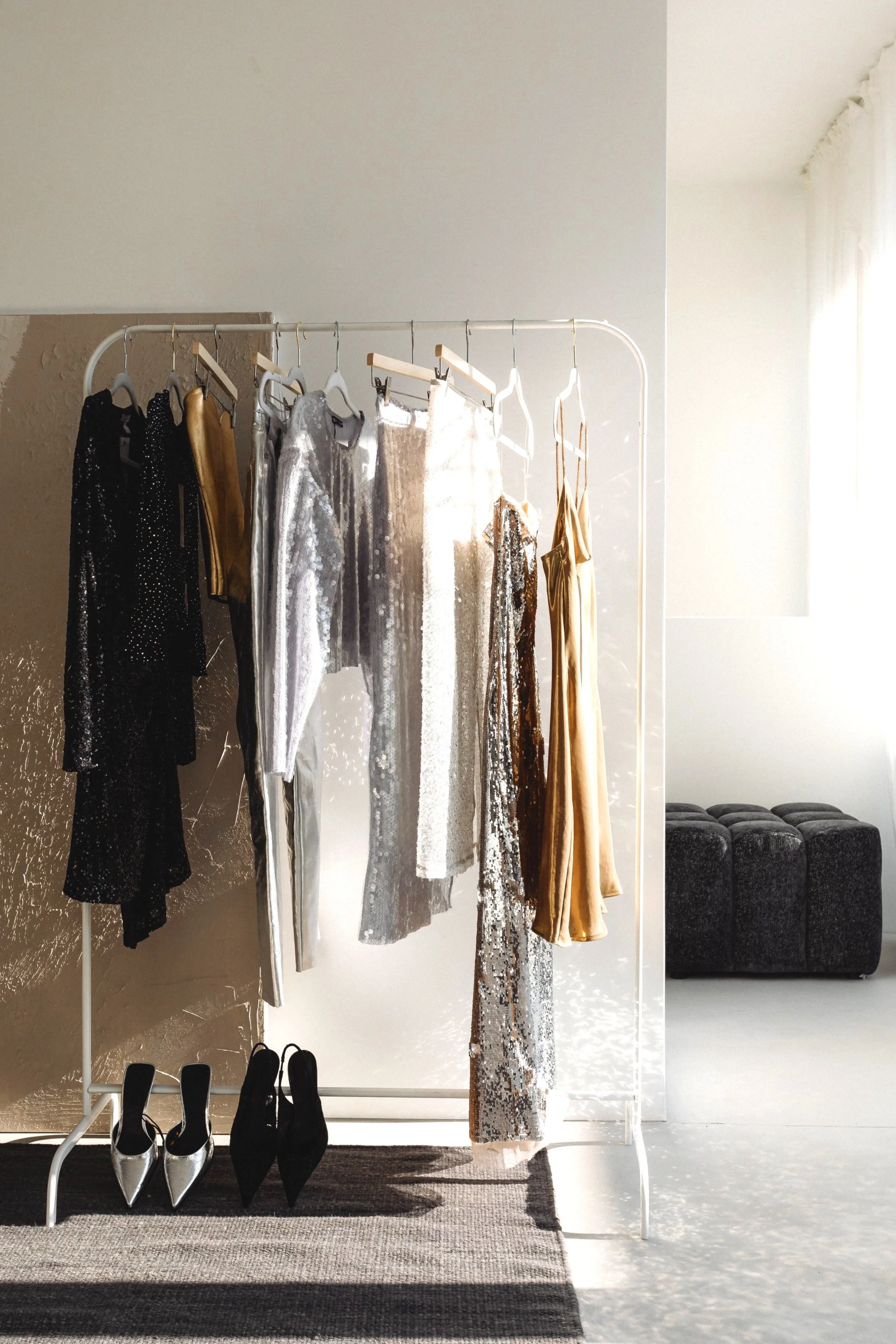 Clothing rack with elegant dresses and shoes in a softly lit room.