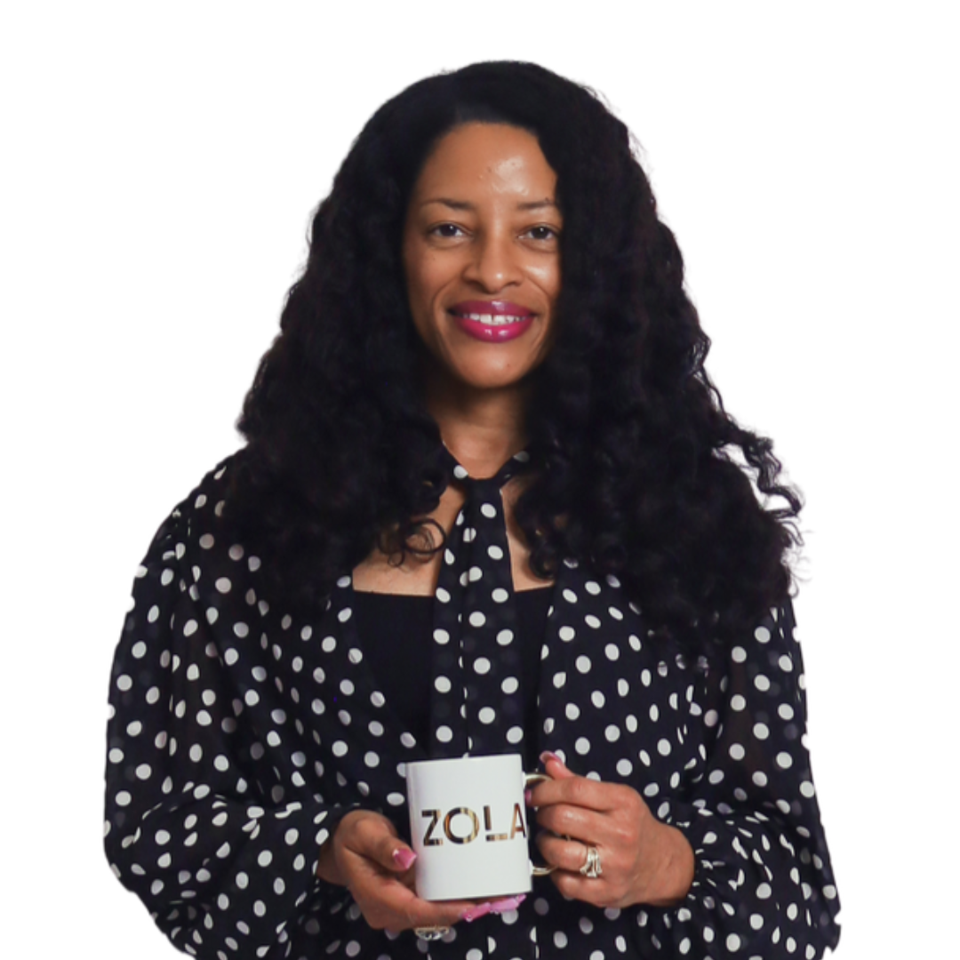 A woman with curly black hair, wearing a light pink T-shirt and purple lipstick, resting her chin on her hand and smiling at the camera.