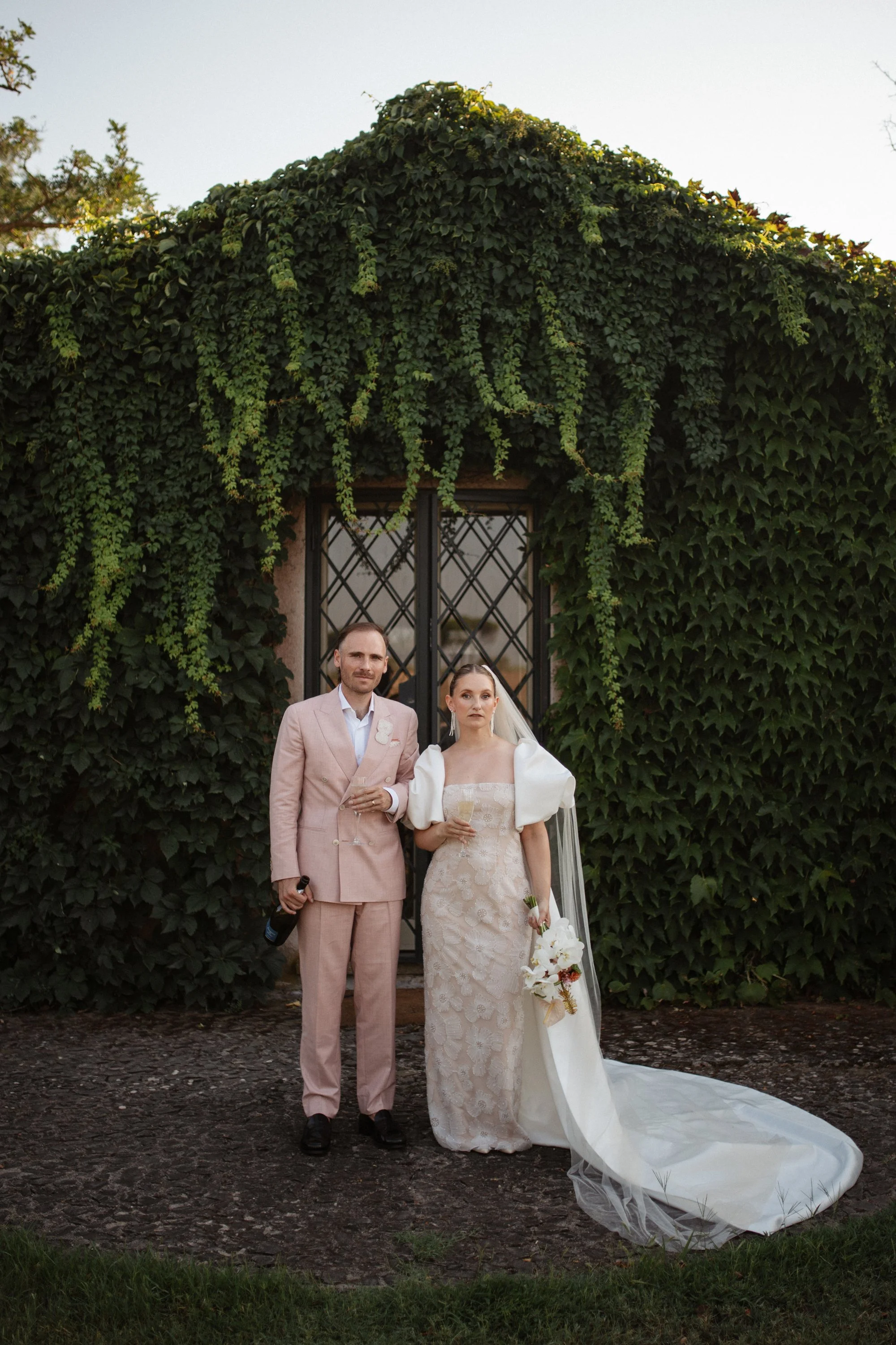 Italian summer wedding at Casale del Gallo near Rome, featuring Selina’s individual wedding dress by Lieben Achten Ehren, her statement cape and Jamie’s rose-colored suit.