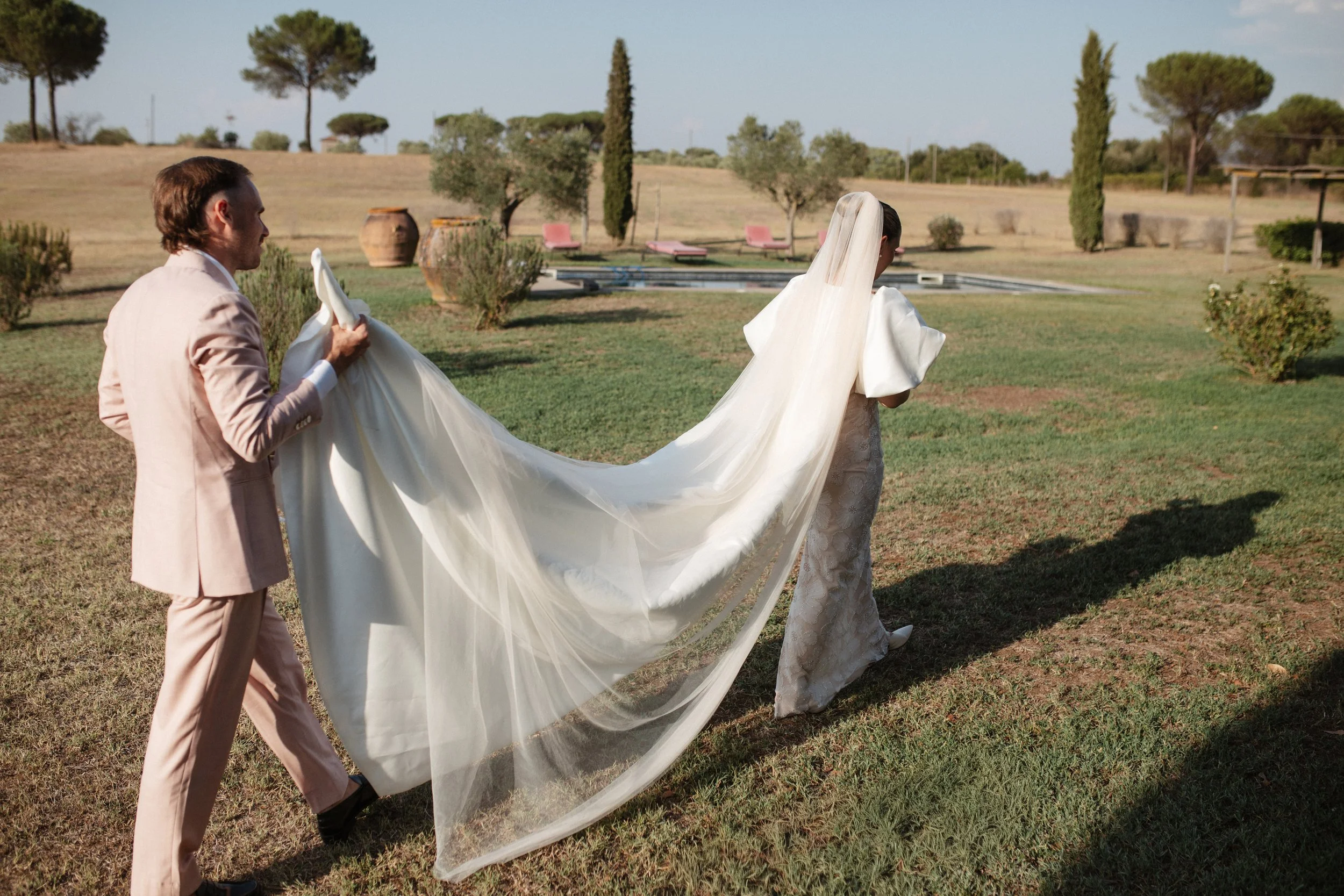 Italian summer wedding at Casale del Gallo near Rome, featuring Selina’s individual wedding dress by Lieben Achten Ehren, her statement cape and Jamie’s rose-colored suit.
