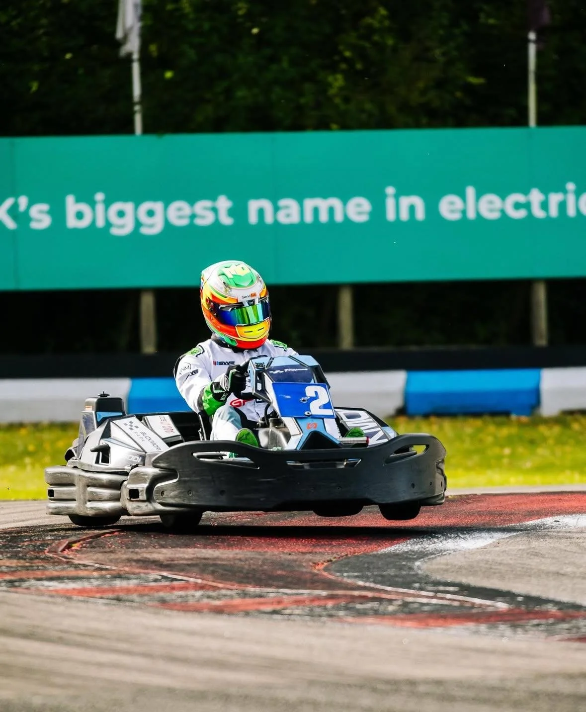 A person in a racing suit and colorful helmet driving a go-kart on a race track.