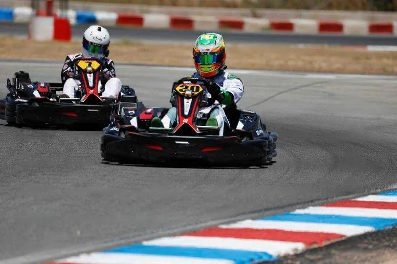 Two go-karts racing on a track with drivers wearing colorful helmets and racing suits.