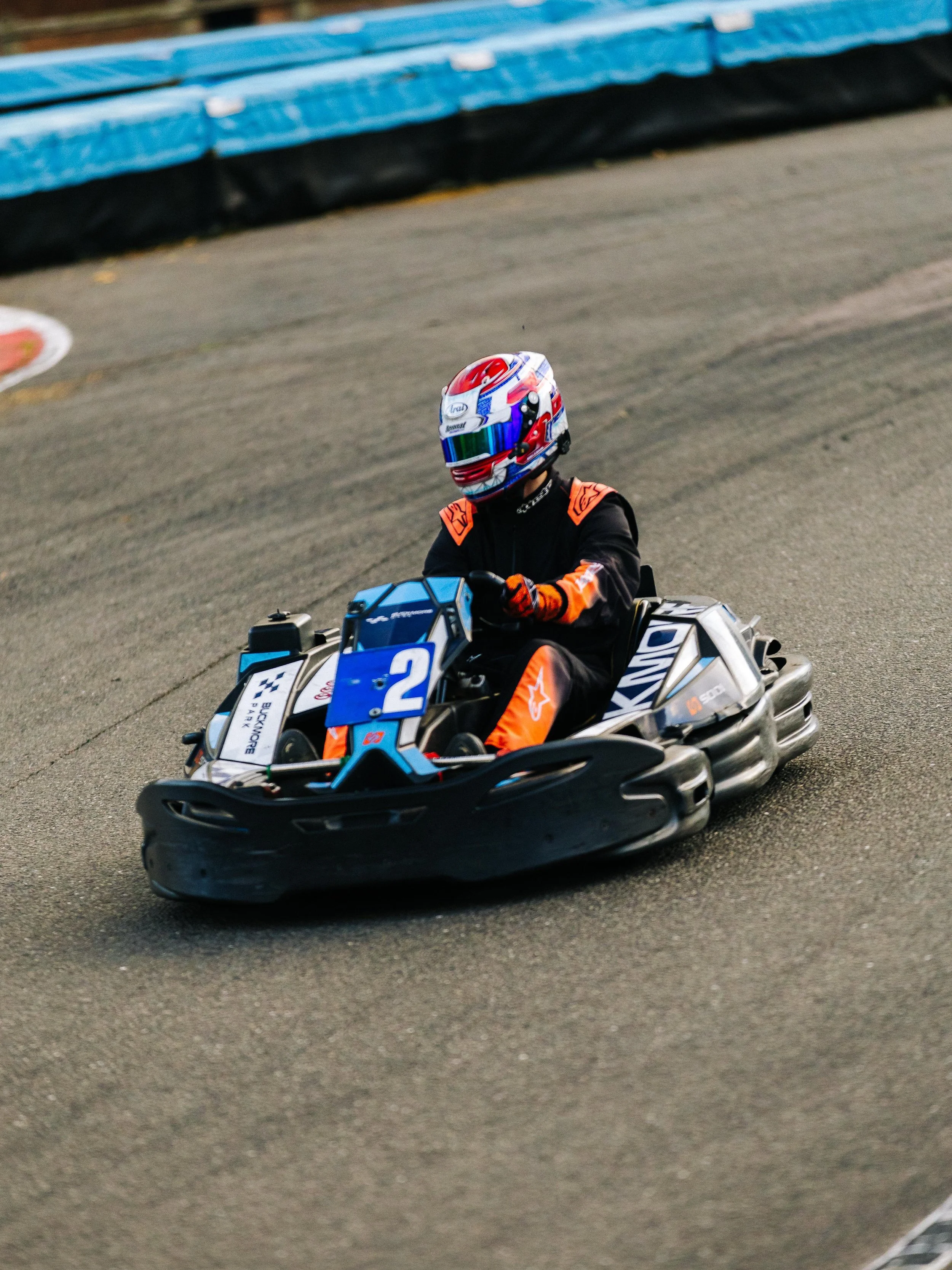 A person in a racing suit and helmet driving a go-kart on a race track.
