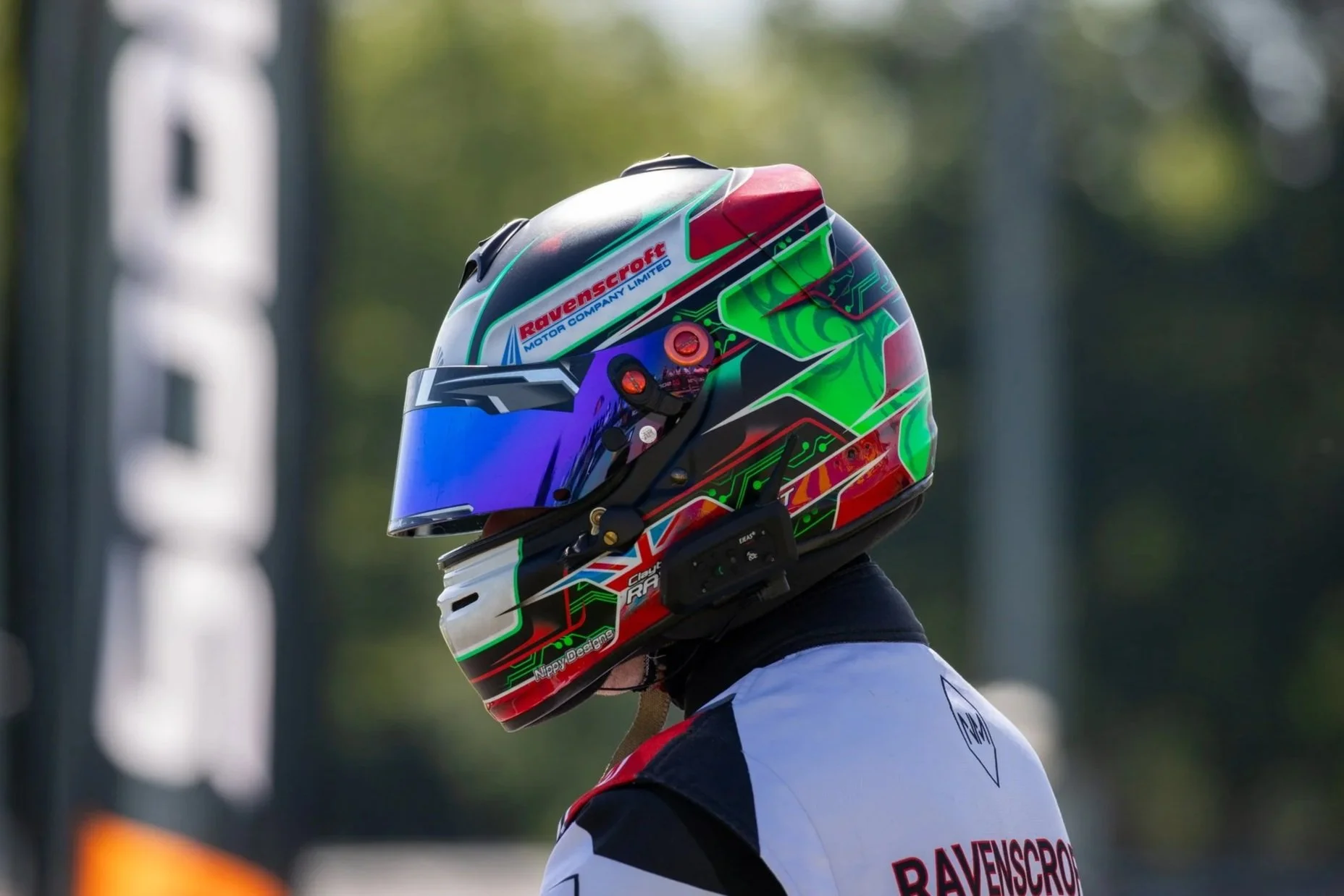 A person wearing a colorful racing helmet with brand stickers and a reflective visor.