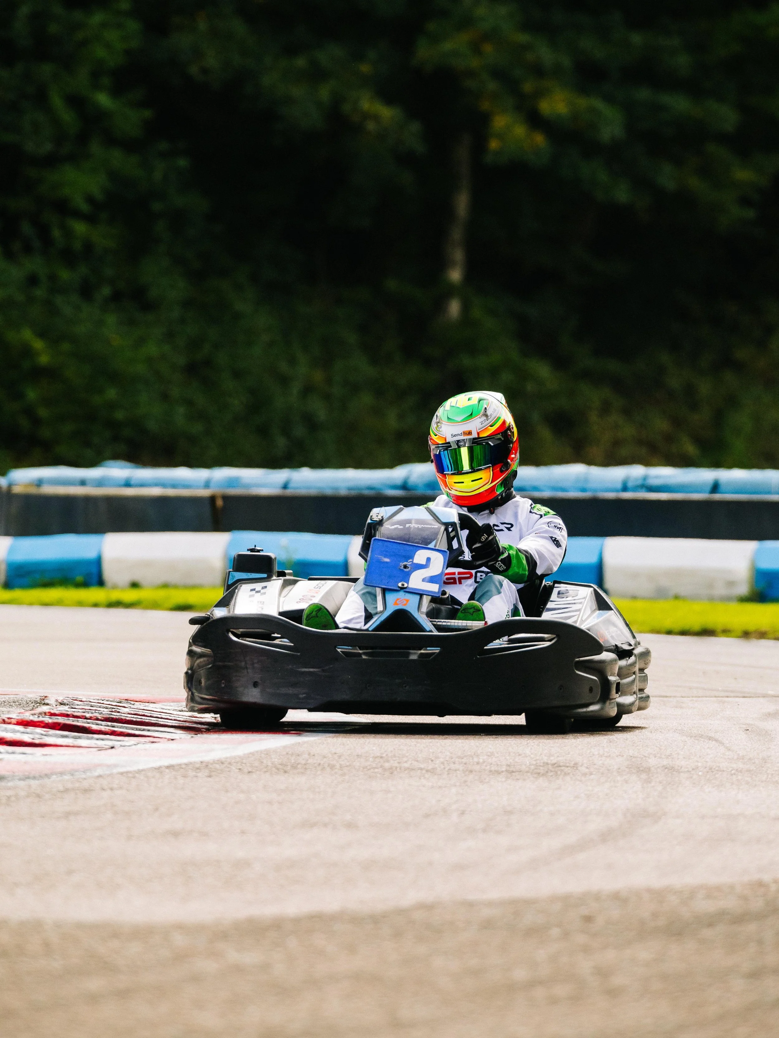 A person racing in a go-kart on a race track, wearing a colorful helmet and racing suit.