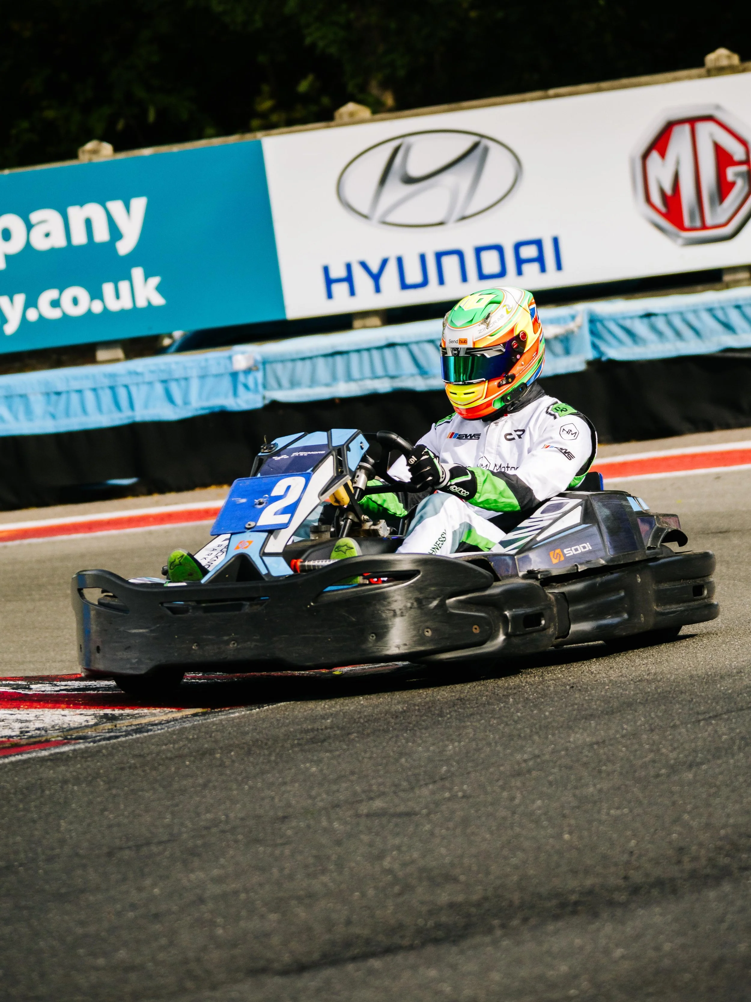 A person in a racing suit and helmet driving a go-kart on a race track.