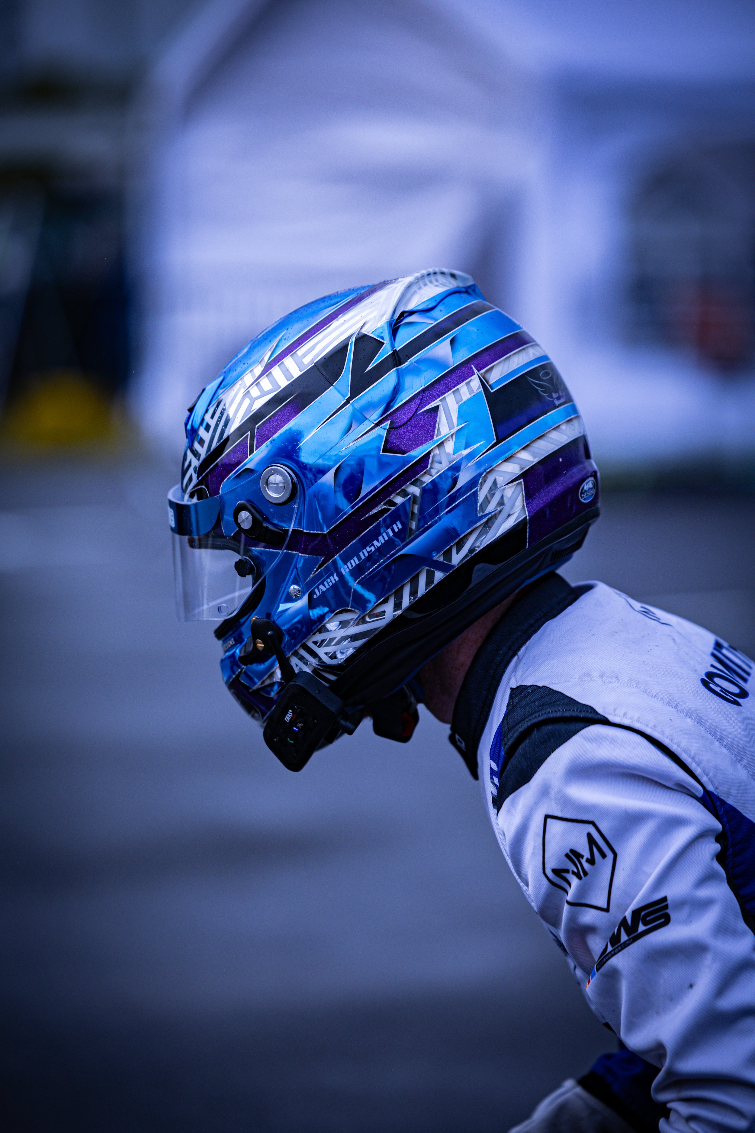 Racing driver in blue and white suit with helmet on a track with green background.
