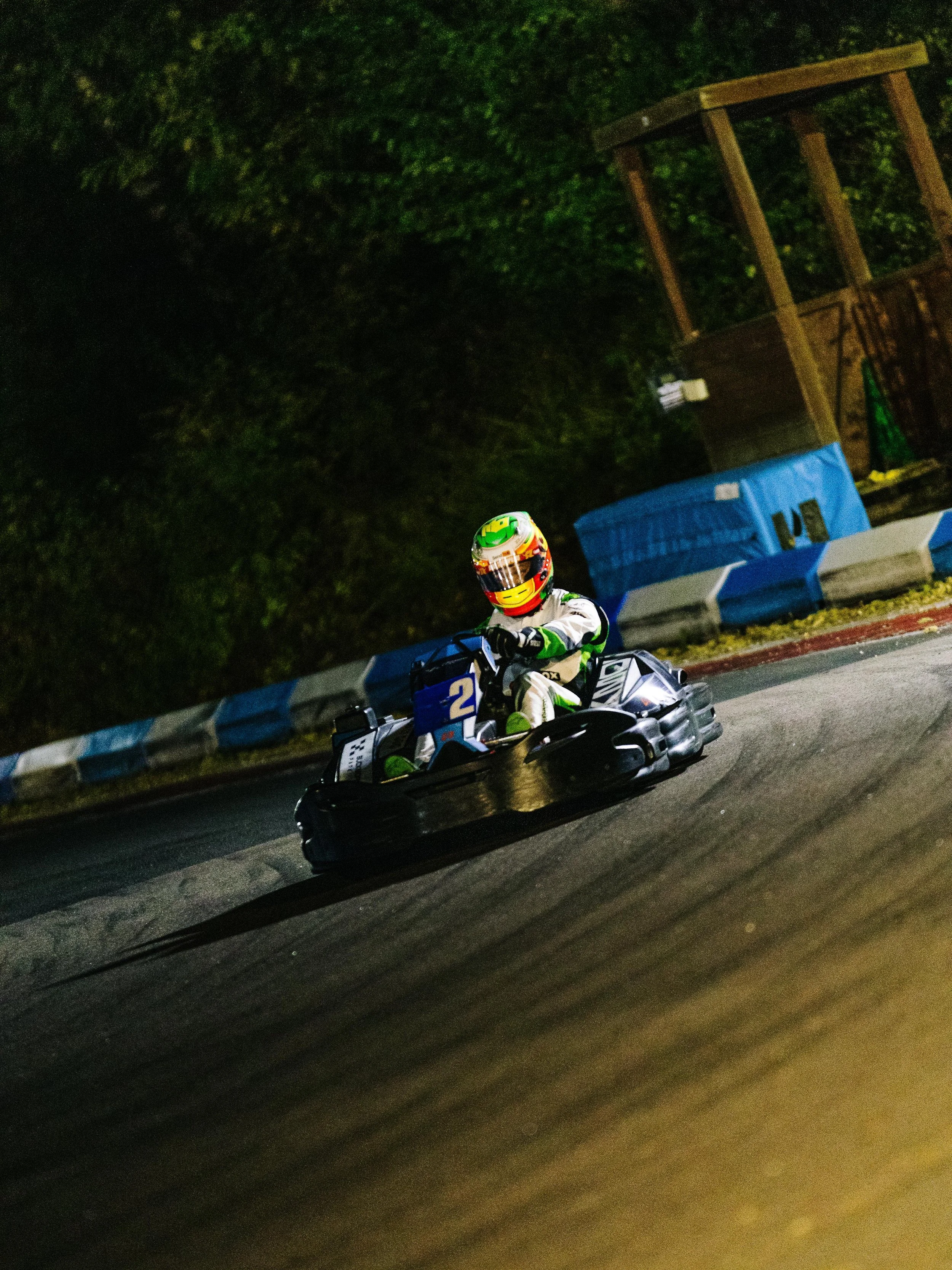 A person wearing a racing suit and helmet driving a go-kart on a race track at night.