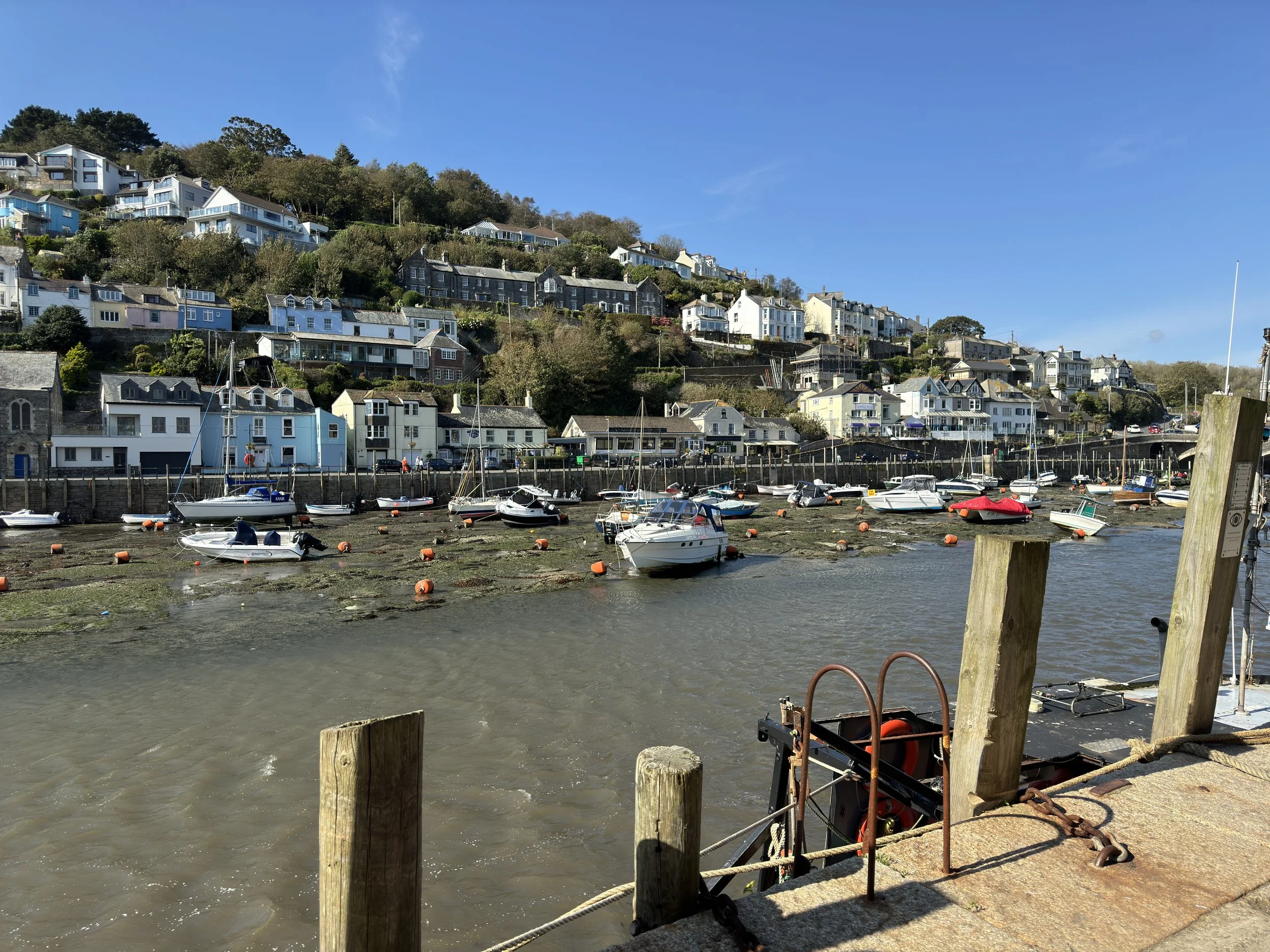 View across Looe Harbour in Cornwall, showing colourful waterfront buildings, fishing boats and the hillside overlooking the town.