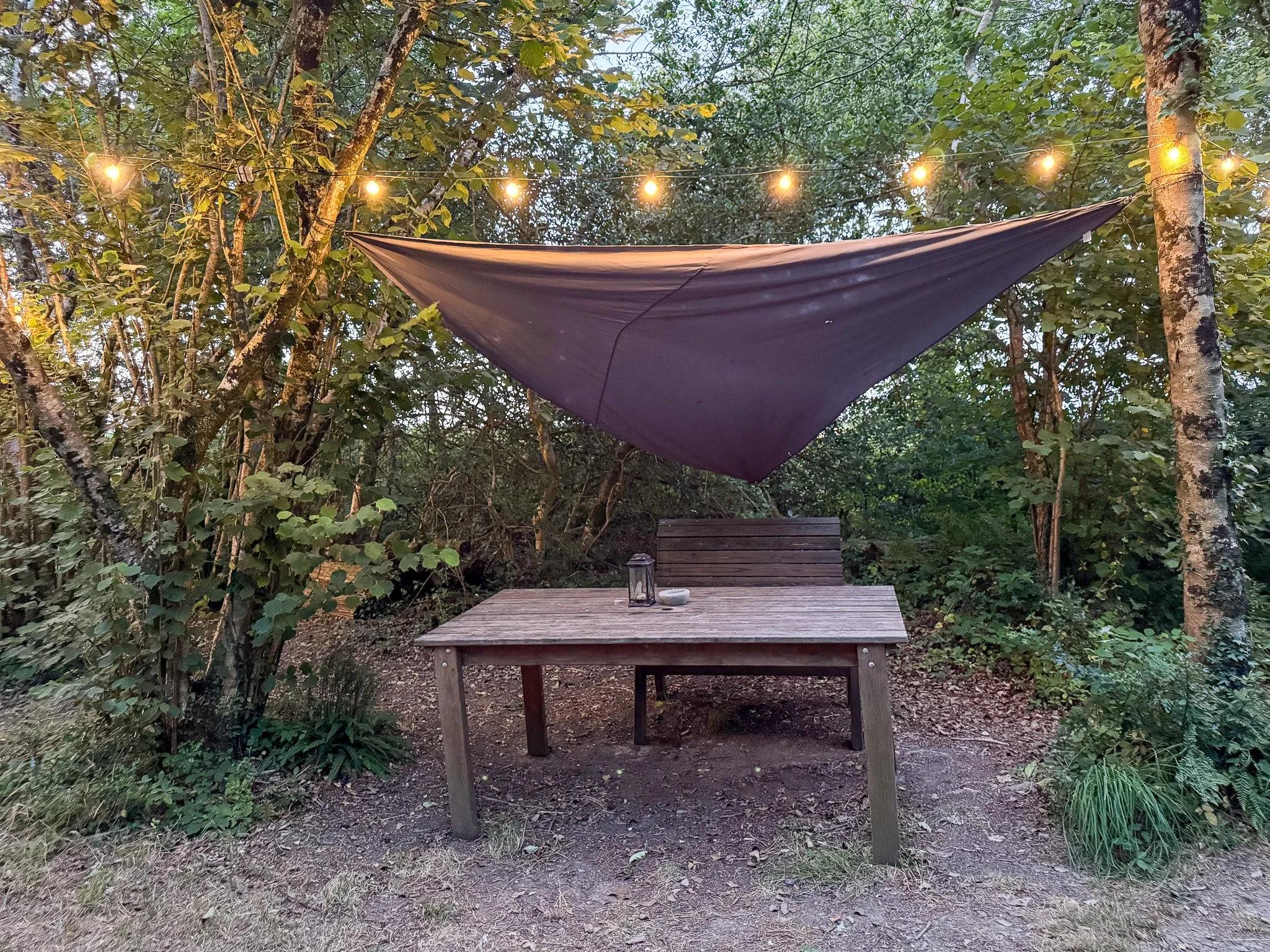 Private outdoor dining area at Slow Glamping in Devon, surrounded by woodland and illuminated with festoon lights.